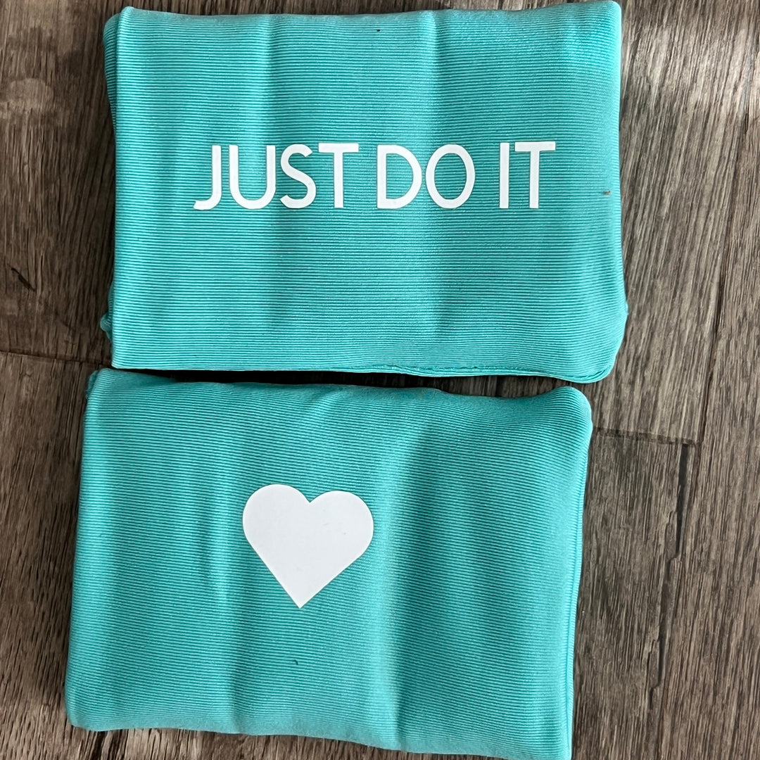 Two teal DRYbands, best wristbands to eliminate rips, on wooden surface, one printed with the vertical text 'JUST DO IT' in white and the other with a white heart shape.