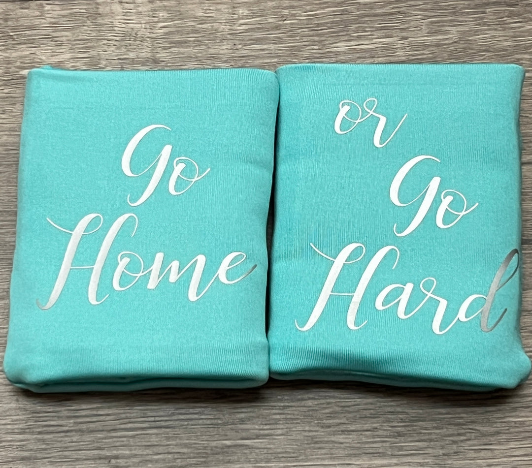 Two teal DRYbands best wristbands for gymnast,  with white script text, placed side by side on a gray wood surface. One reads "Go Home" and the other reads "or Go Hard.