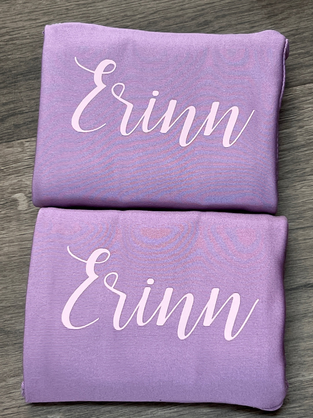 Two lavender DRYbands, best wristbands for gymnasts, with the name 'Erinn' printed in white script, displayed on a gray wood-textured surface.