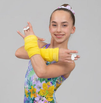 A young gymnast girl posing with yellow DRYbands, best wristbands for gymnasts, against a solid gray background.